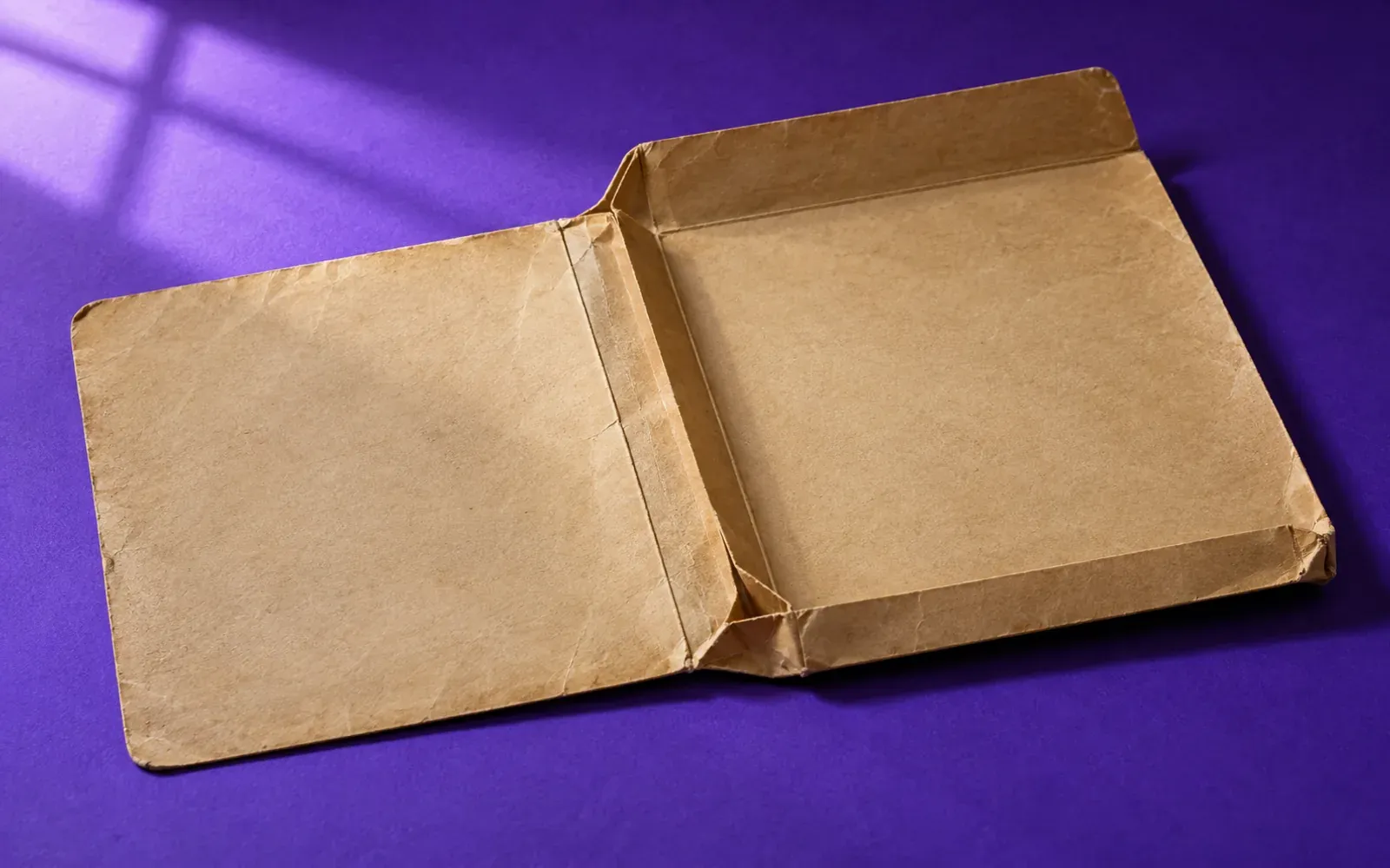 An empty buff document wallet lying open and flat on a deep violet surface, its gusset creased from long use, nothing inside.